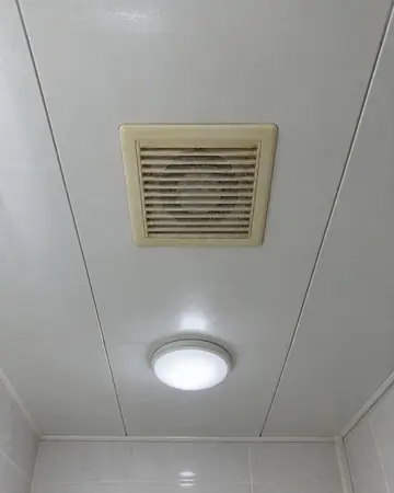 욕실 천장의 낡은 환풍기 덮개와 주변 천장판, 옆 조명이 함께 나온 사진 (참고용 생성 이미지)